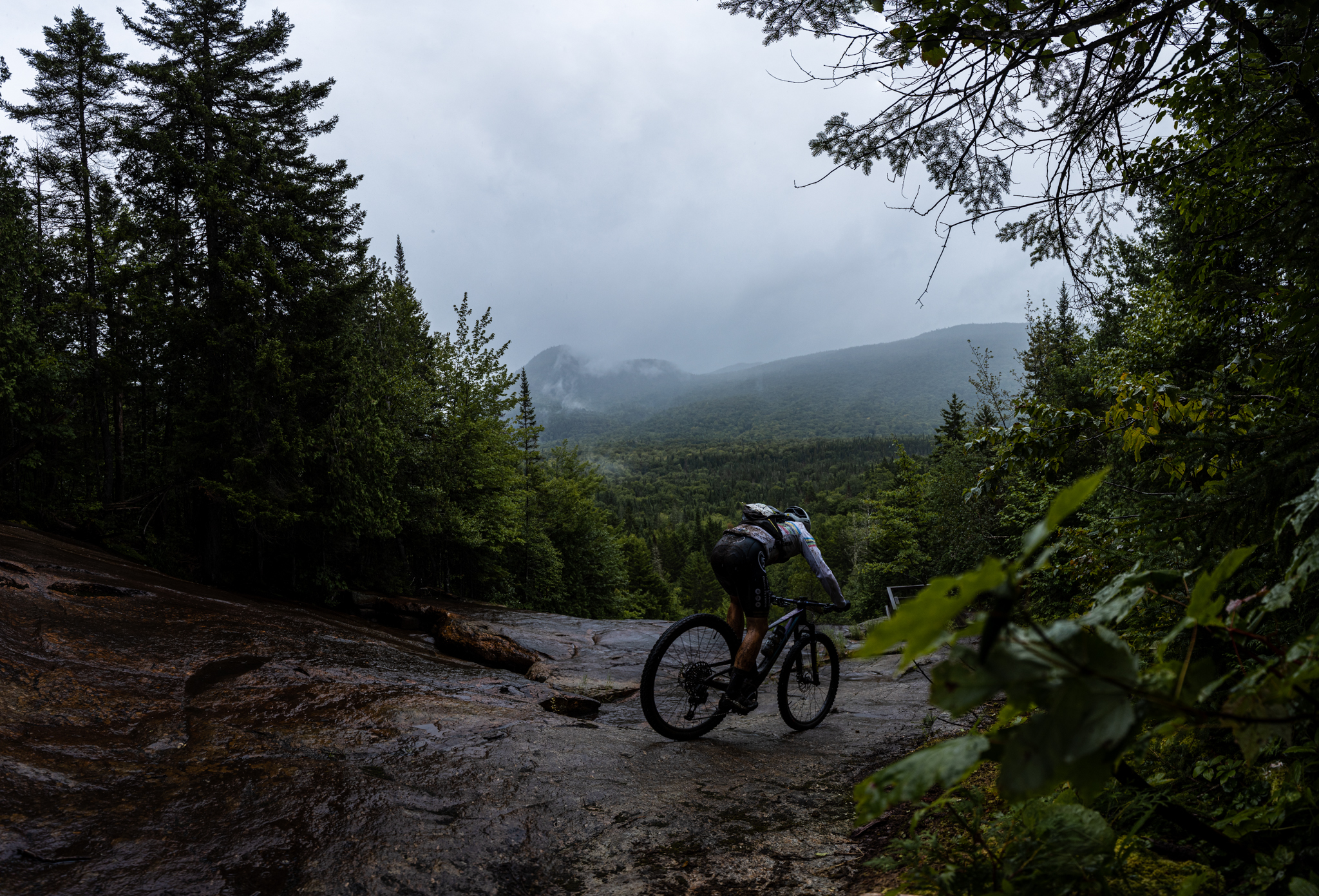 A cyclist enjoying the outdoor sport of mountain biking on the Légende trail, one of the most epic trails in Quebec, under the cloud cover of the surrounding mountains.