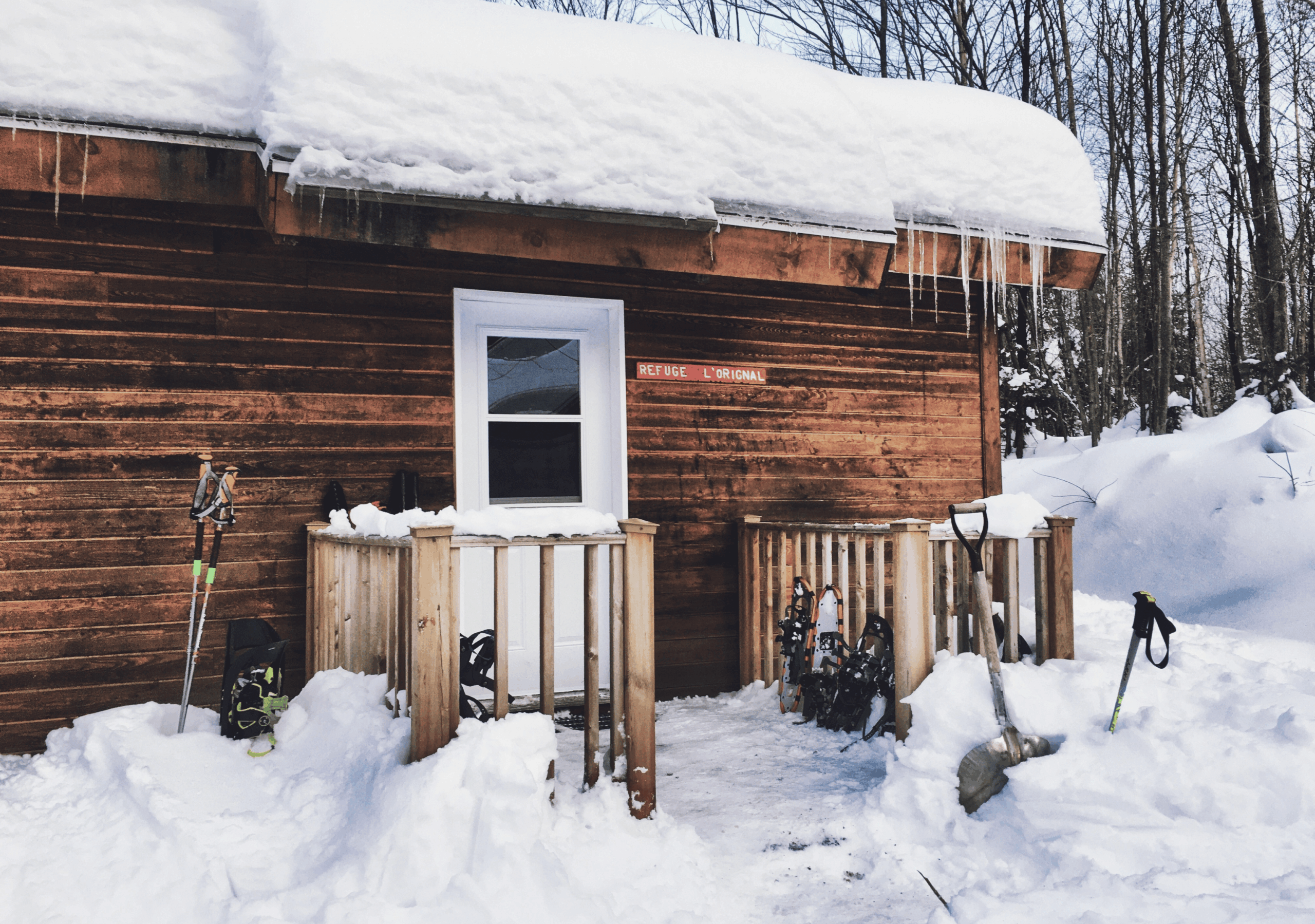 Refuge rustique en bois couvert de neige, pelle et raquettes sur la galerie