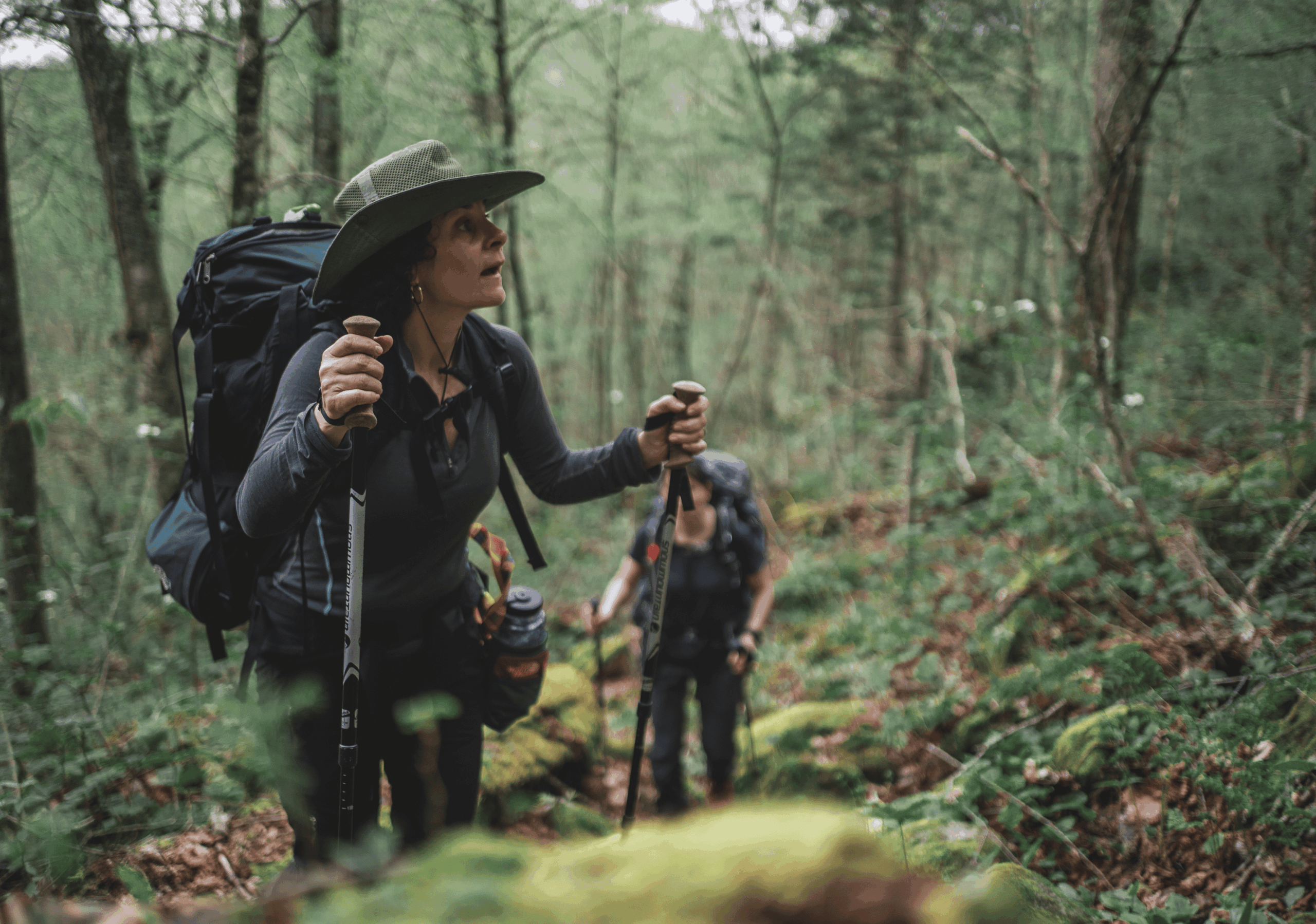 Randonneuse portant un chapeau et utilisant des bâtons de marche, regardant vers l'avant en sentier