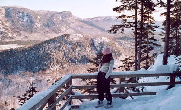 Une jeune femme admirant le paysage hivernal, des montagnes au lac gelé, par une tour d'observation, accessible par l'un des sentiers de randonnées hivernales offerts par la Vallée.