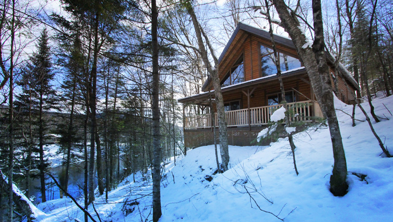 View of the snow-covered façade of one of the chalets offered by Chalets Etsanha, Partenaire à la Vallée, surrounded by forest and winter nature. This chalet is ideal for both summer and winter stays.