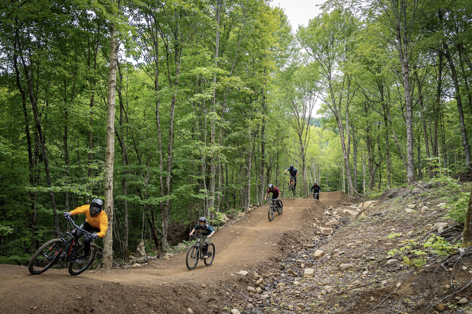 Un groupe de cyclistes pratiquant une activité de plein air, le vélo de montagne, et s'aventurant sur l'un des sentiers les plus épiques du Québec, le Godzilla, idéal pour amateurs d'aventures en pleine nature.