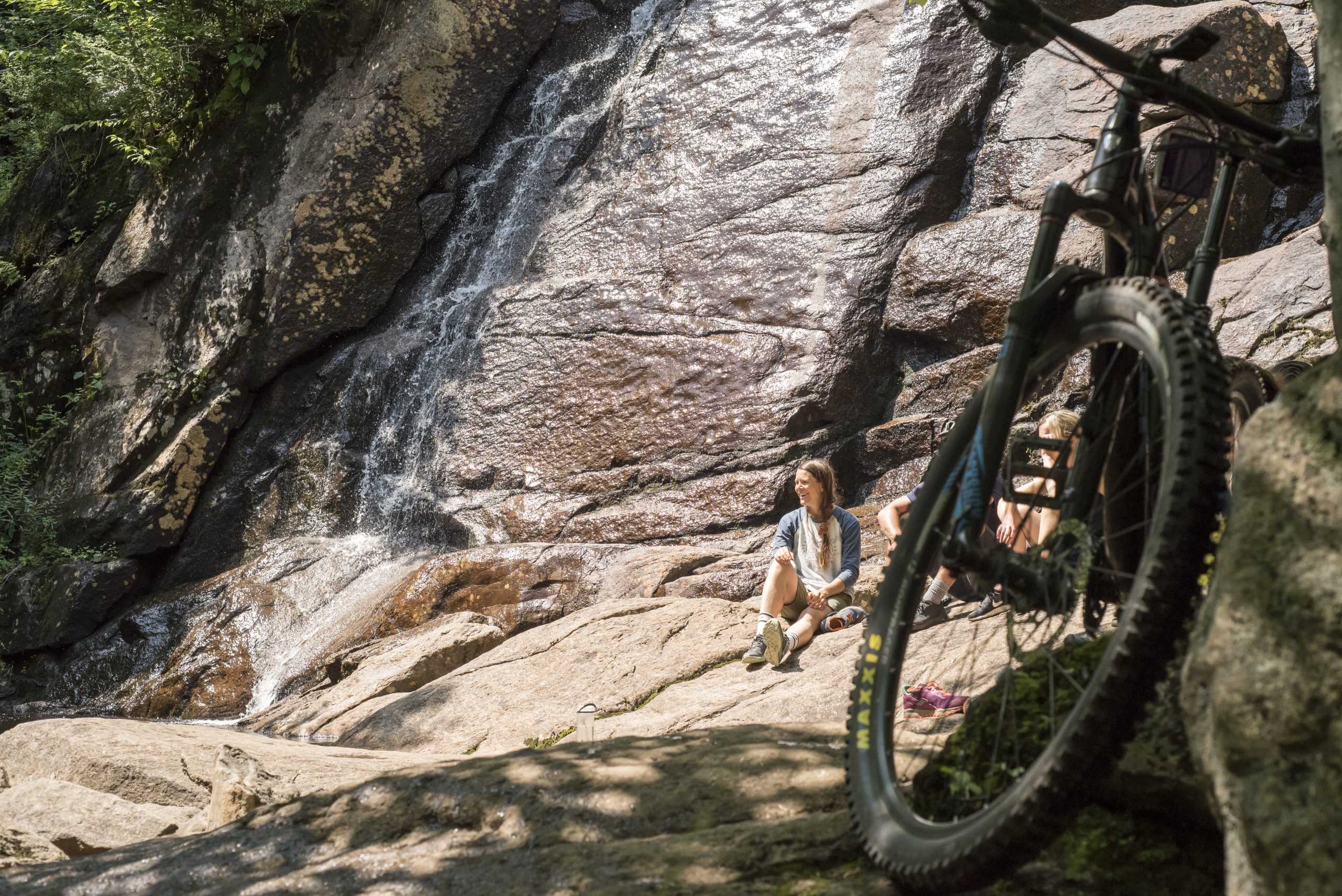 Two cyclists taking a break at the foot of Chute à Gilles, with their mountain bikes in the foreground.