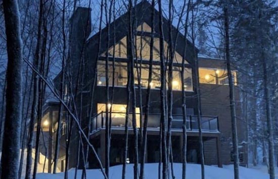 Winter and evening facade of the Chalet du Domaine Passerelle, a Partner chalet in the Valley, surrounded by snow-covered forest and nature.