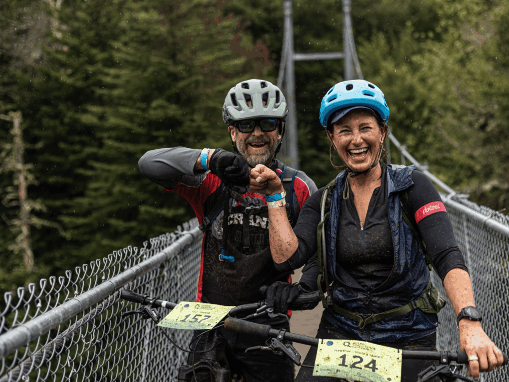 Deux adeptes de vélo de montagne souriants, couverts de boue après une sortie sous la pluie à la Vallée Bras-du-Nord.