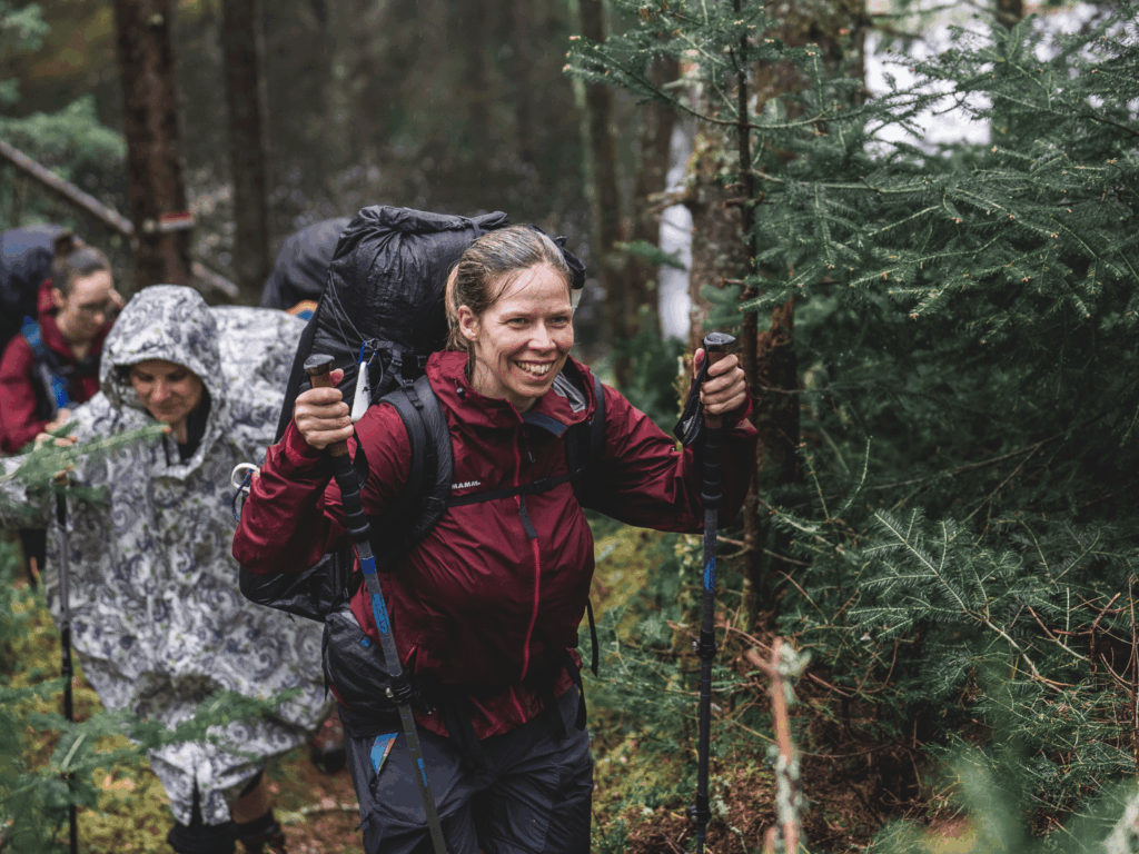 Groupe de randonneurs progressant en forêt sous une pluie légère, bien équipés pour une aventure en plein air malgré la météo.